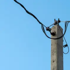 Betonowy słup energetyczny z kablami na tle błękitnego nieba. Zastanawiasz się, ile wynosi odszkodowanie za słupy energetyczne na działce?