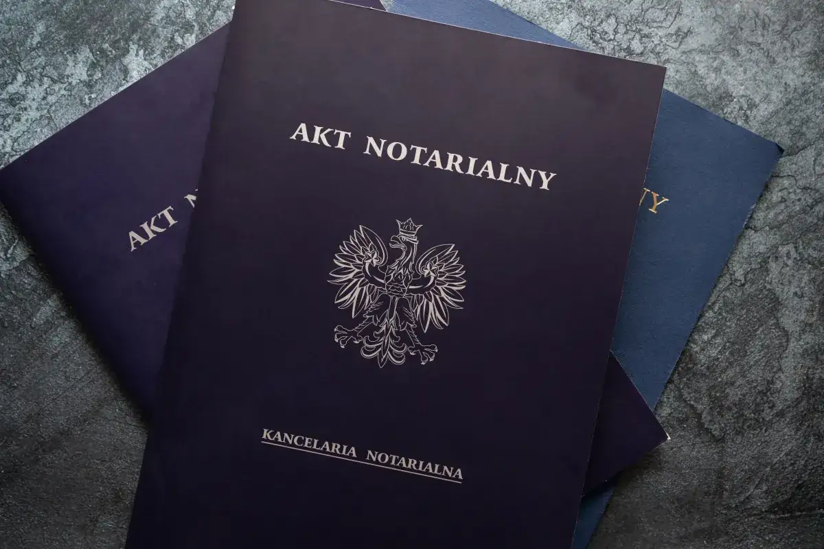 Stos dokumentów, w tym akt notarialny z godłem Polski, gotowy do podpisania.